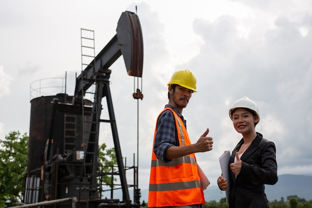 Female engineers consult with workers next to working oil pumps with a sky .