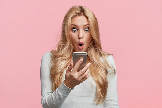 Female enterpreneur or businesswoman being disappointed with news from colleague, reads message on smartphone, shocked to recieve responsibility prepare difficult project for tomorrow`s meeting