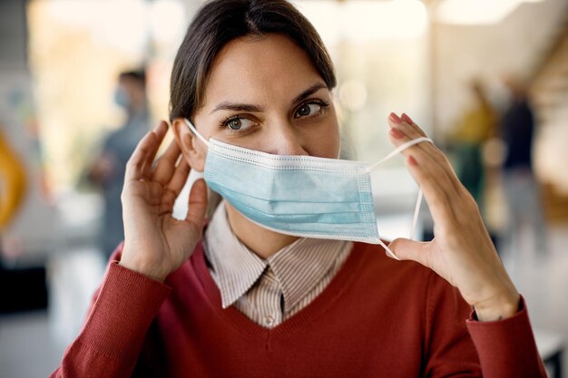 Female entrepreneur putting on a face mask while working in the office