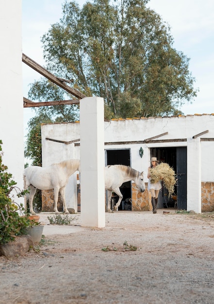 Free Photo female farmer carrying hay for her horses