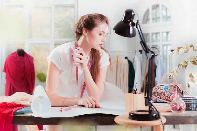 Free photo the female fashion designer working in studio sitting on the desk