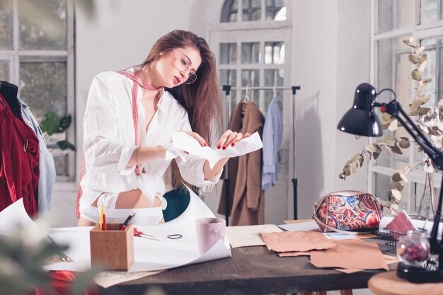 The female fashion designer working in studio sitting on the desk