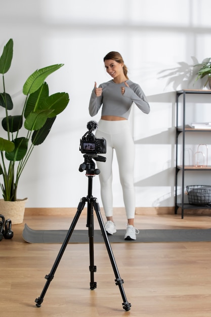 Free photo female fitness instructor teaching an online class from home using a camera on tripod