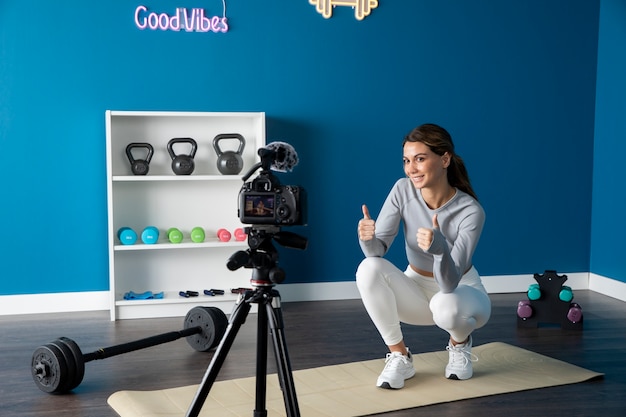 Free Photo female fitness instructor teaching an online class from home using a camera on tripod