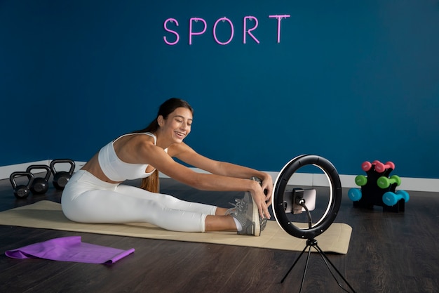 Female fitness instructor working out at home in front of ring light