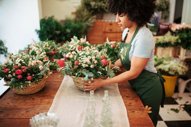 Female florist arranging basket of flowers on wooden desk