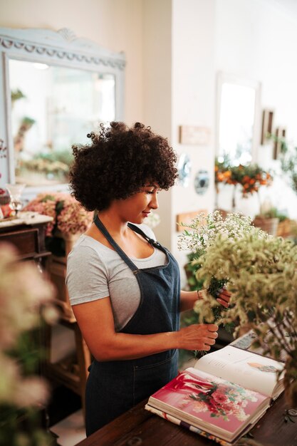 Female florist holding bunch of flower plant with photo album on desk