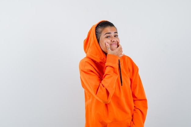 Female forcing a smile on face in orange hoodie and looking weird 