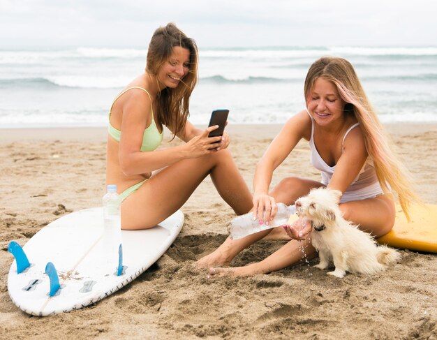 Female friends at the beach with dog and smartphone