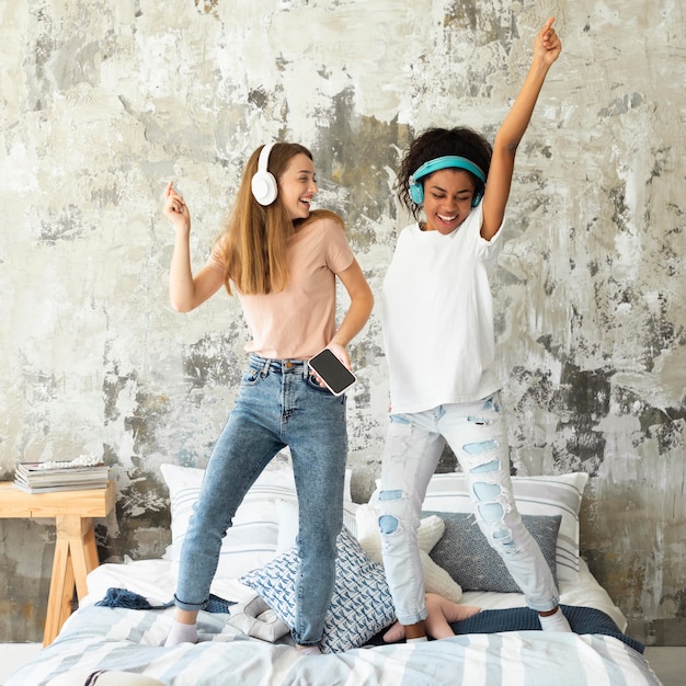 Free photo female friends dancing in bed while listening to music on headphones