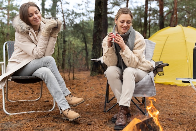 Free photo female friends drinking water by a bonfire during camp