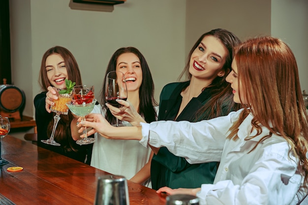 Free Photo female friends having a drinks at bar. they are sitting at a wooden table with cocktails.