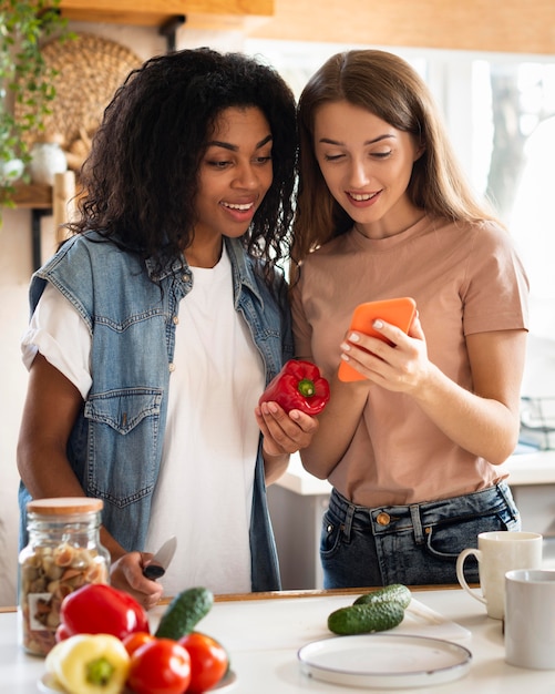 Female friends in the kitchen with smartphone and vegetables