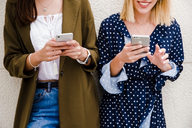 Free Photo female friends leaning on wall using smartphone