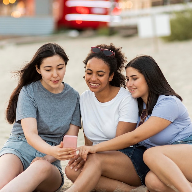 Female friends sitting on the beach with smartphone