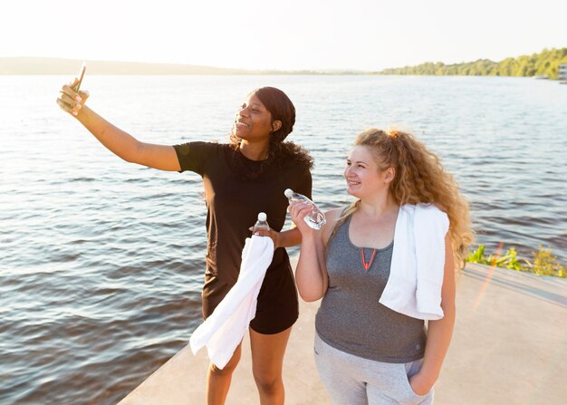 Female friends taking selfie together while exercising by the lake