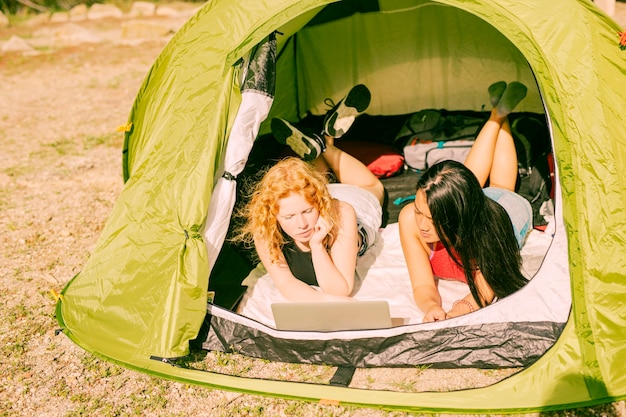 Female friends in tent using laptop