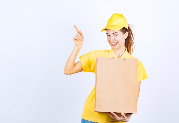 Female girl in yellow uniform holding a cardboard shopping bag and pointing at somewhere. 