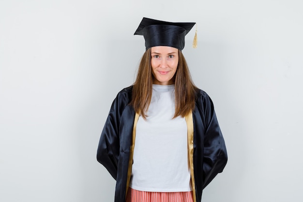 Free photo female graduate keeping hands behind back in uniform, casual clothes and looking ashamed , front view.