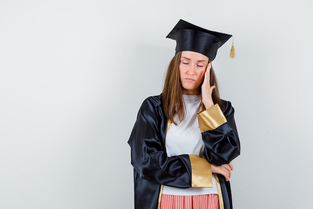 Female graduate in uniform, casual clothes having headache and looking exhausted , front view.