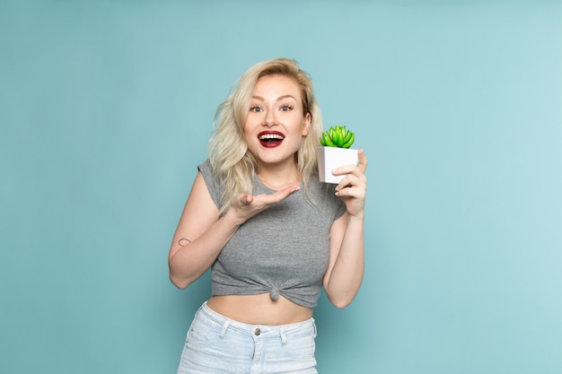 female in grey shirt and bright blue jeans holding little plant