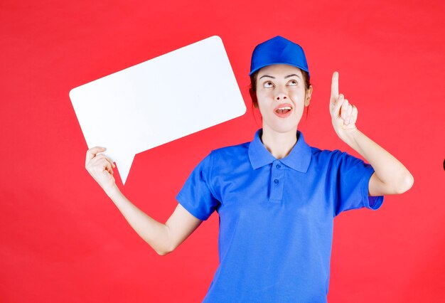 Female guide in blue uniform holding a white rectangular info board. 