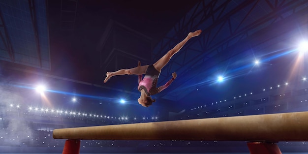 Female gymnast doing a complicated trick on gymnastics balance beam in a professional arena