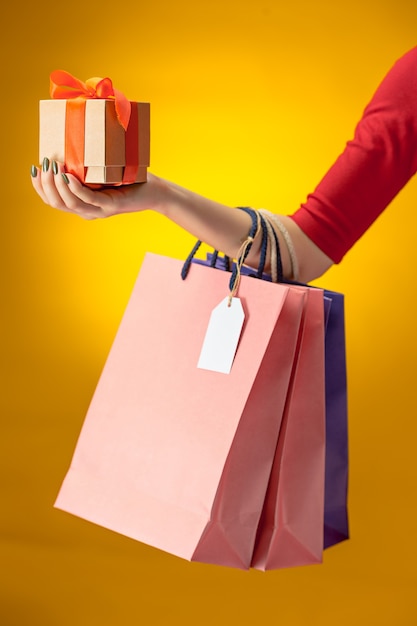 Free photo female hand holding bright shopping bags on yellow