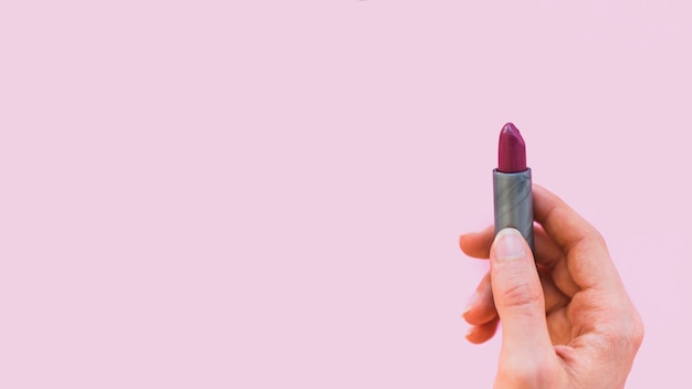 Free Photo female hand holding dark shade lipstick on pink background