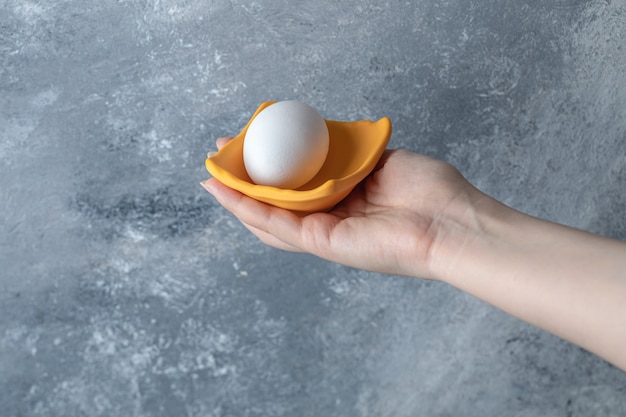 Female hand holding egg in yellow bowl.