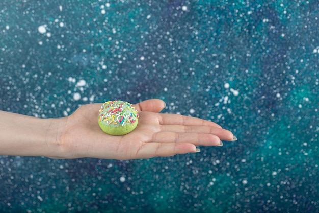 Free photo female hand holding green cookie with sprinkles.