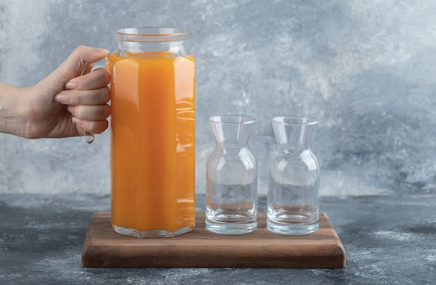 Female hand holding jug of orange juice. 