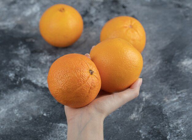 Female hand holding oranges on marble table. 