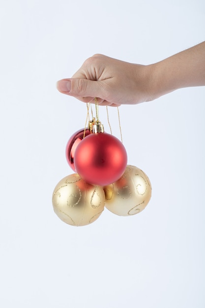 Female hand holding shiny Christmas baubles on white surface