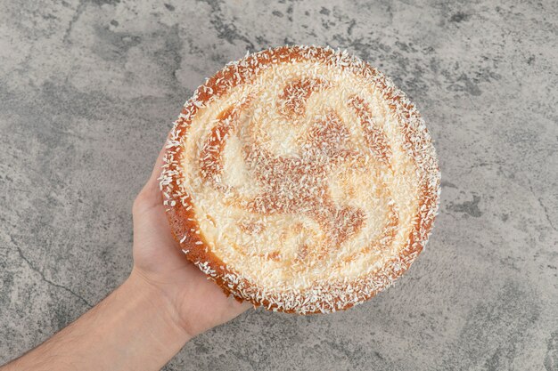 Female hand holding sweet apple pie on marble surface. 