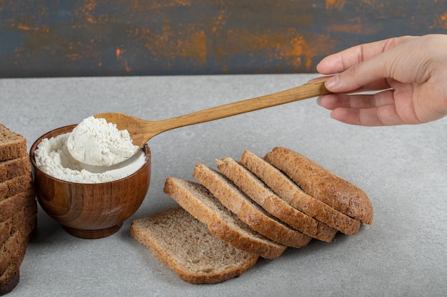 Female hand holding a wooden spoon of flour and slices of bread.