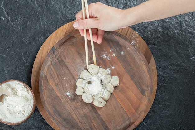 Female hand taking dumpling with chopsticks from plate.