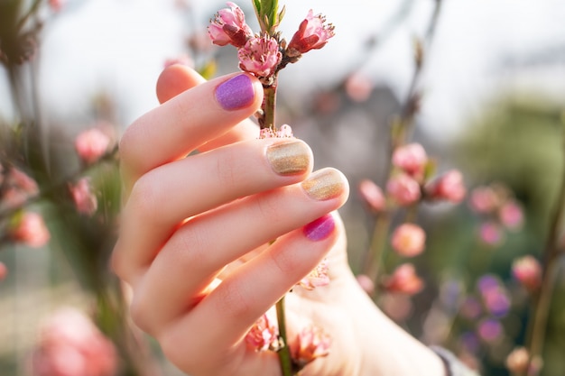 Free Photo female hand with gold and purple nail design holding blossom branch.