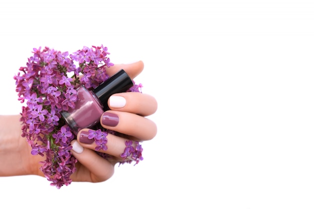 Female hand with white and purple nail design holding lilac flowers