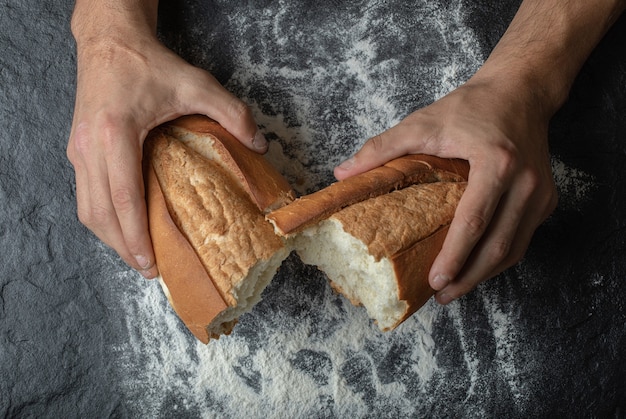 Free photo female hands breaking freshly baked bread, top view.