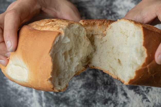 Female hands close-up breaking fresh baguette bread.