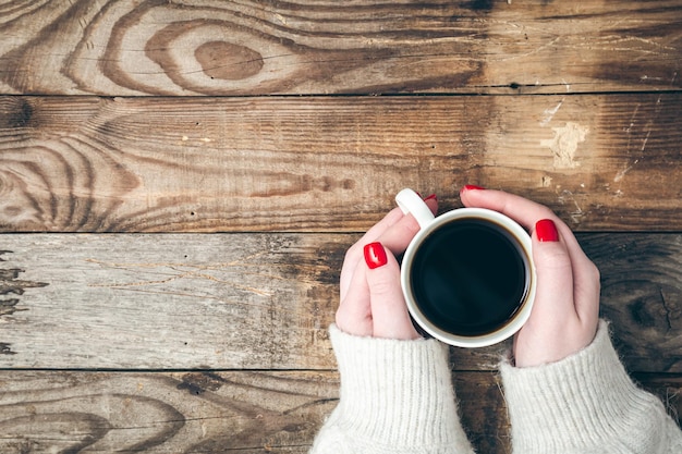 Free photo female hands hold a cup of coffee on a wooden background flat lay