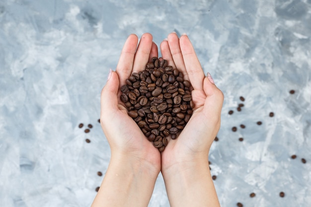 Female hands holding coffee beans flat lay on a grungy grey background