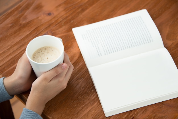 Free Photo female hands holding coffee cup on table with book