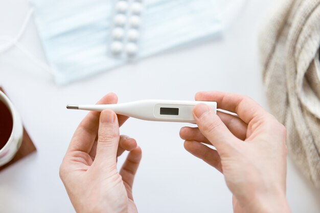 Female hands holding electronic thermometer over the white offic