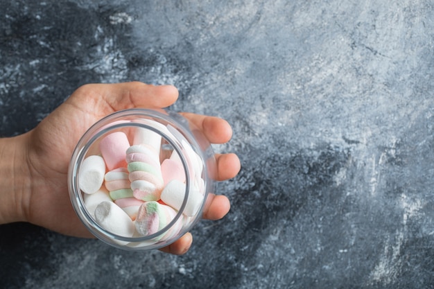 Free Photo female hands holding glass jar of marshmallows on marble background