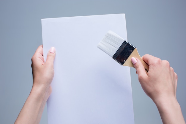 female hands holding painting brush on white canvas