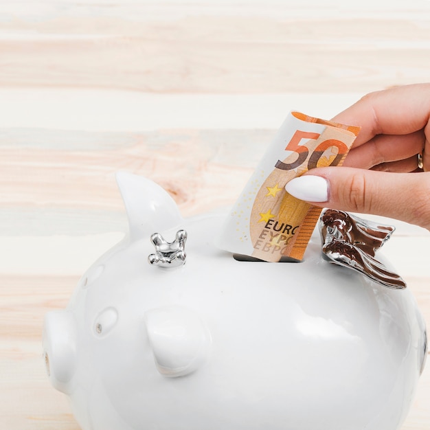 Female hands inserting fifty euro note in the white piggybank