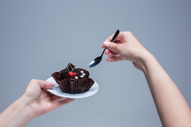 Free photo female hands keeping cake with spoon on gray