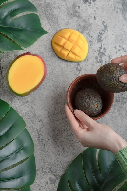 Free photo female hands picking ripe avocados from bowl on marble surface.